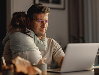 Man holding child while checking computer